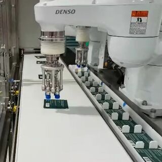 Close-up of Denso robotic arm picking circuit boards from a conveyor line